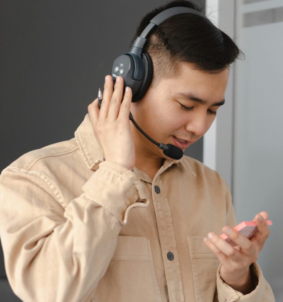 Asian man wearing headset, consulting with clients, holding notes in front of sticky notes.
